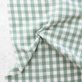 close up of white and sage green gingham fabric from the brand "fableism"